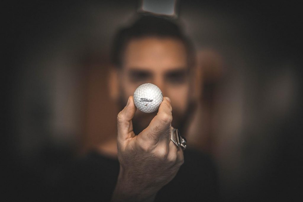 Mann blickt konzentriert & fokussiert auf einen Golfball.